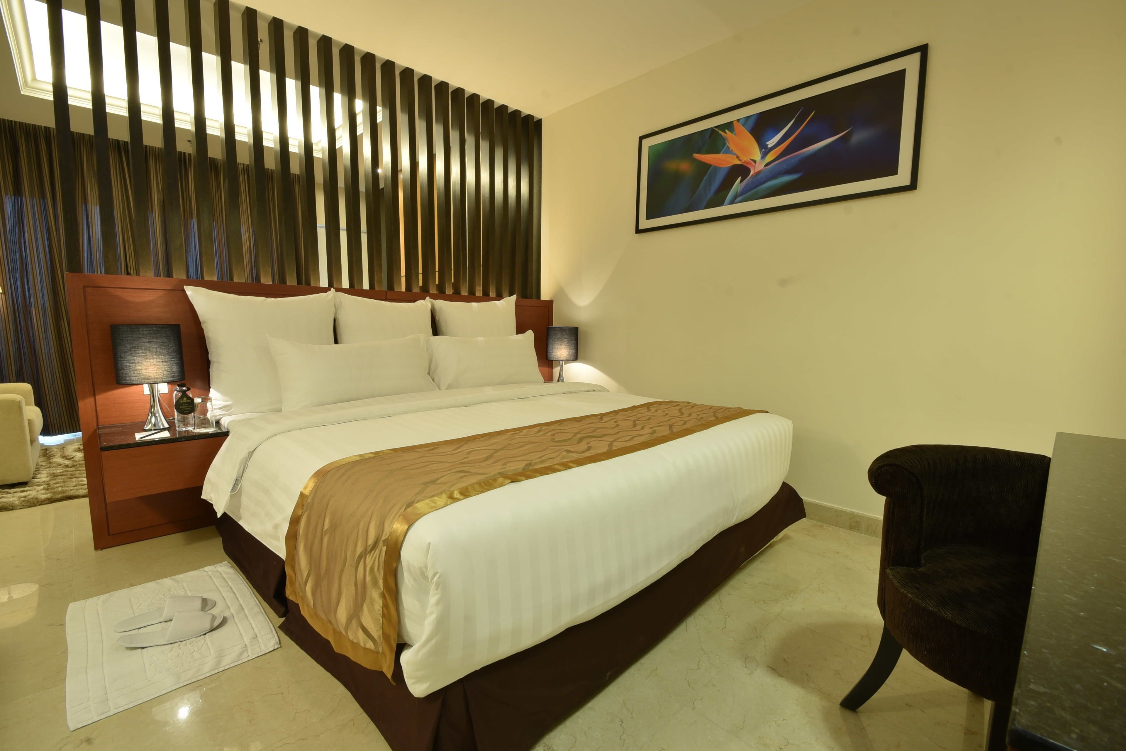 A hotel room with a large bed, a nightstand with a lamp, a chair, and a painting on the wall.