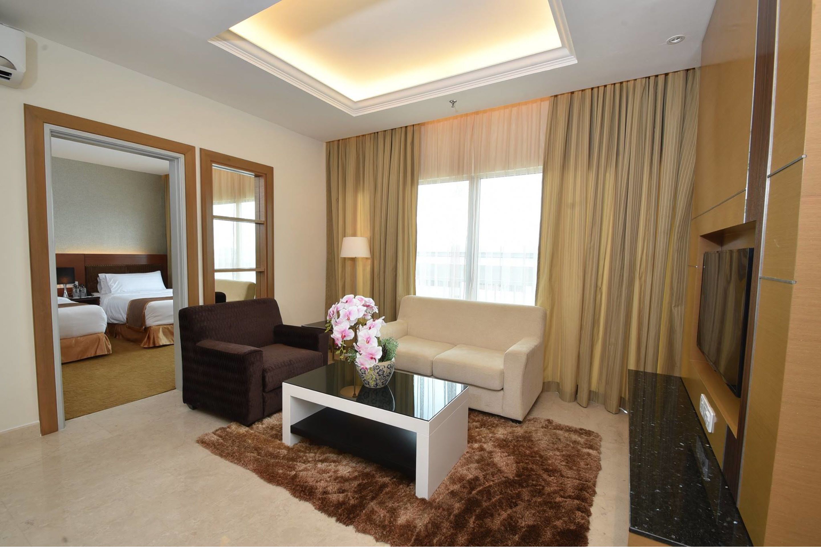 A hotel room with a bed, a sofa, a coffee table, a TV, and a large window with curtains.