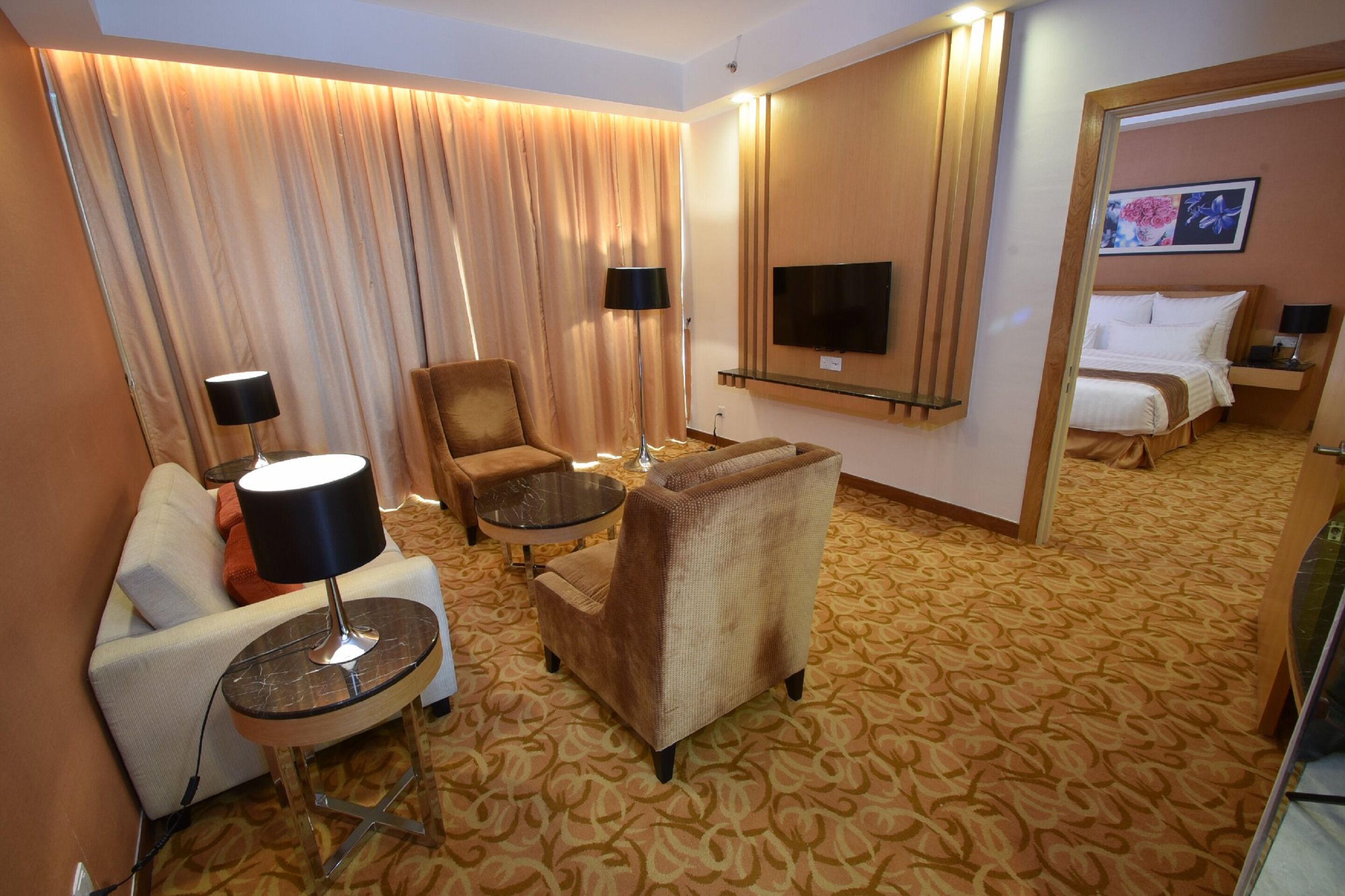 Ein Hotelzimmer mit einer Couch, einem Sessel, einem runden Tisch und einem Bett mit angebautem Fernseher.