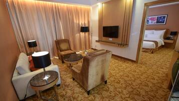 Ein Hotelzimmer mit einer Couch, einem Sessel, einem runden Tisch und einem Bett mit angebautem Fernseher.