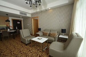 Habitación de hotel con alfombra estampada, un sofá, una pequeña mesa, zona de comedor y candelabro.