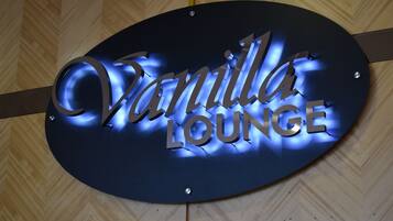 A sign for "Vanilla Lounge" with illuminated letters against a wooden background.