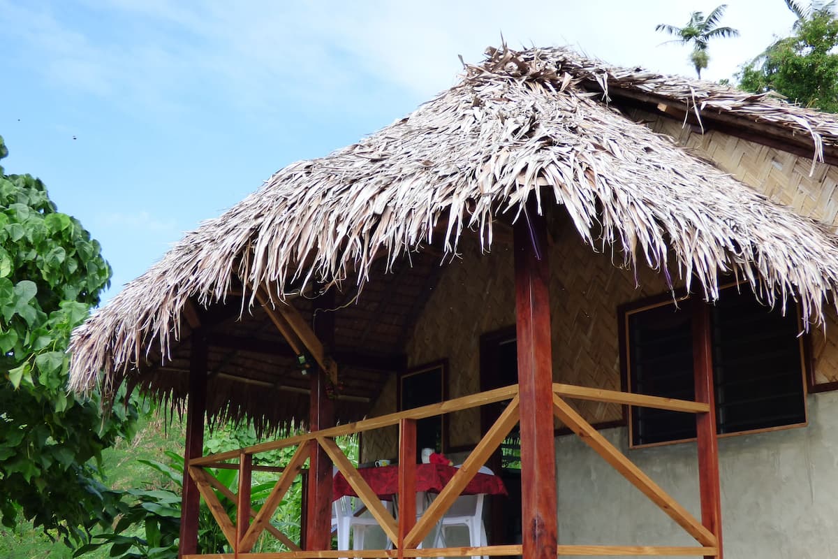 A thatched-roof structure with a wooden balcony, surrounded by greenery.