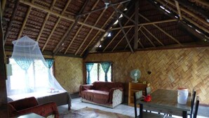 A room with a thatched roof, a bed with a mosquito net, a sofa, a dining table with chairs, and a fan. - Malekula Holiday Villas (Lakatoro)