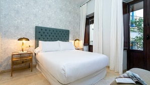 Un dormitorio ordenado con una cama grande, dos mesitas de noche con lámparas, una ventana con cortinas y vistas al exterior.