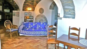 A cozy living room with a blue patterned sofa, wooden chairs, a dining table, and stone arches.
