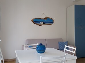 Un comedor con una mesa blanca, un florero azul y una obra de arte colgada en la pared.