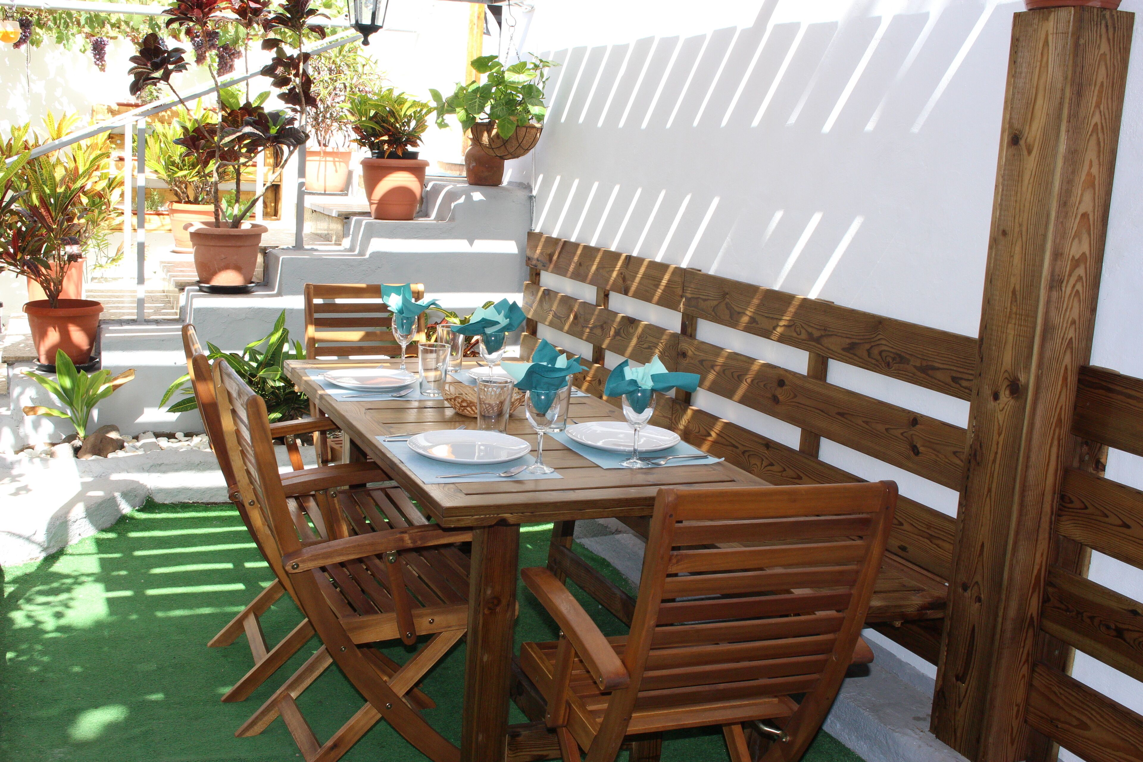 An outdoor dining area with a wooden table set for four, surrounded by wooden chairs.