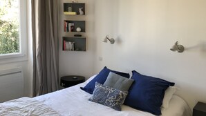 A bedroom with a bed, pillows, a nightstand, a wall-mounted shelf with books and a lamp, and a window with curtains. - Biarritz, T2 45 m² near Côte des Basques (Biarritz)