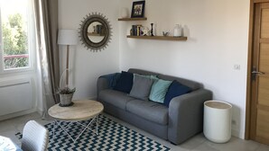 A living room with a grey sofa, a round mirror, a small table, and a patterned rug. - Biarritz, T2 45 m² near Côte des Basques (Biarritz)