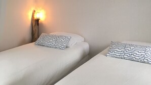 A room with two beds, each with a patterned pillow, a wall-mounted light fixture, and a sloped ceiling. - Sea view from the large beach (Quiberon)
