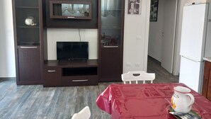 Sala de estar com televisão, móvel de entretenimento de madeira e uma mesa vermelha com caneca e sachês.