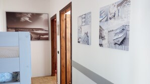 Um corredor com chão de azulejos, portas de madeira e obras de arte nas paredes retratando barcos e cenas náuticas.