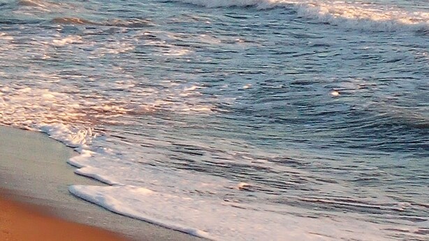 Uma praia com ondas e colinas ao longe.