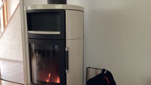 Una stufa a legna moderna con sportello in vetro, una combinazione di colori bianco e nero, e una piccola panca di legno con un cappello accanto.