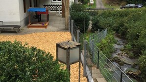 Un edificio con una zona salotto esterna coperta, un sentiero che conduce a un ruscello e un giardino recintato.