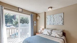 A bedroom with a large bed, a nightstand with a lamp, a window with a view of trees, and a ceiling light fixture. - 37sll - Economical - Convenient - Kitchenette - Sleeps 2 1 Bedroom Condo by RedAwning (Deming)
