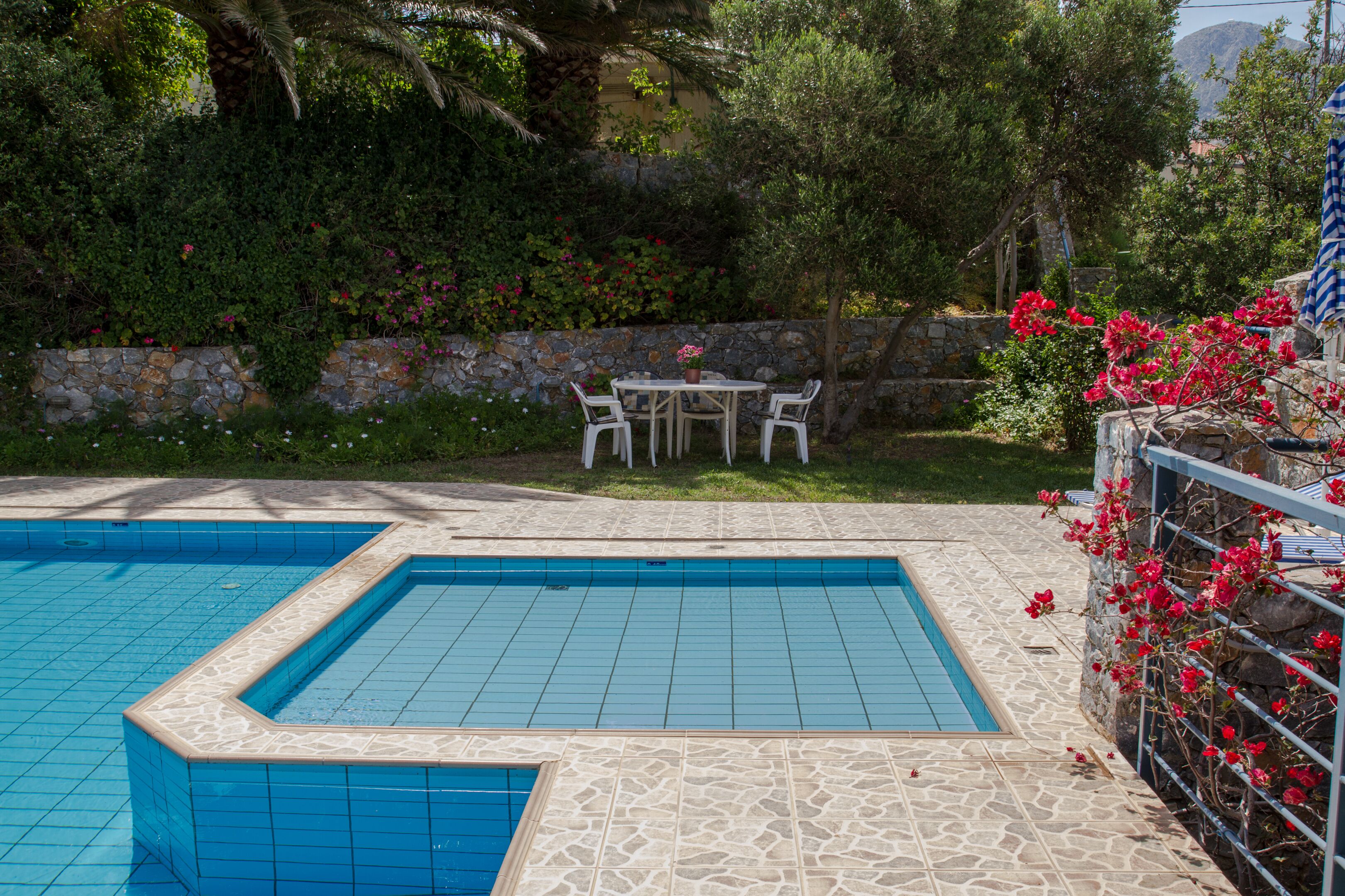 Una piscina amb dues zones, terrassa de pedra i taula amb cadires.