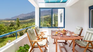 Un balcon avec une table et des chaises en bois, une vue sur un paysage montagneux et un plafond bleu et blanc.
