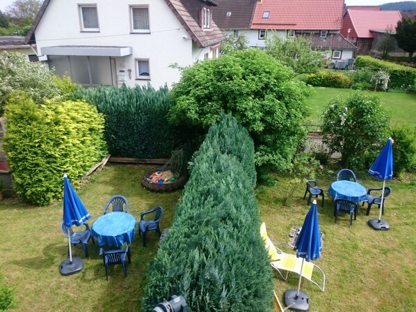 A well-maintained garden with a variety of trees and shrubs, outdoor seating with umbrellas, and a white house in the background. - 6 bed apartment near the old imperial city of Goslar. Wicki's Biker Lodge (Langelsheim)