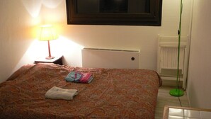 A neatly made bed with a patterned bedspread, a folded towel, and a lamp on a bedside table.
