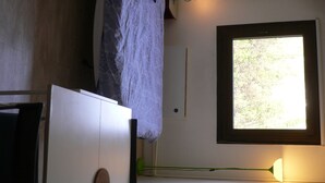 A room with a bed, a window with a view of trees, a white cabinet, and a green lamp.
