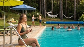 A swimming pool with people, a hammock, and a table with drinks.
