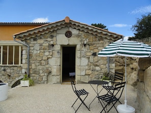 Un bâtiment en pierre avec un toit en tuiles, une porte et un petit porche comprenant une table et des chaises.