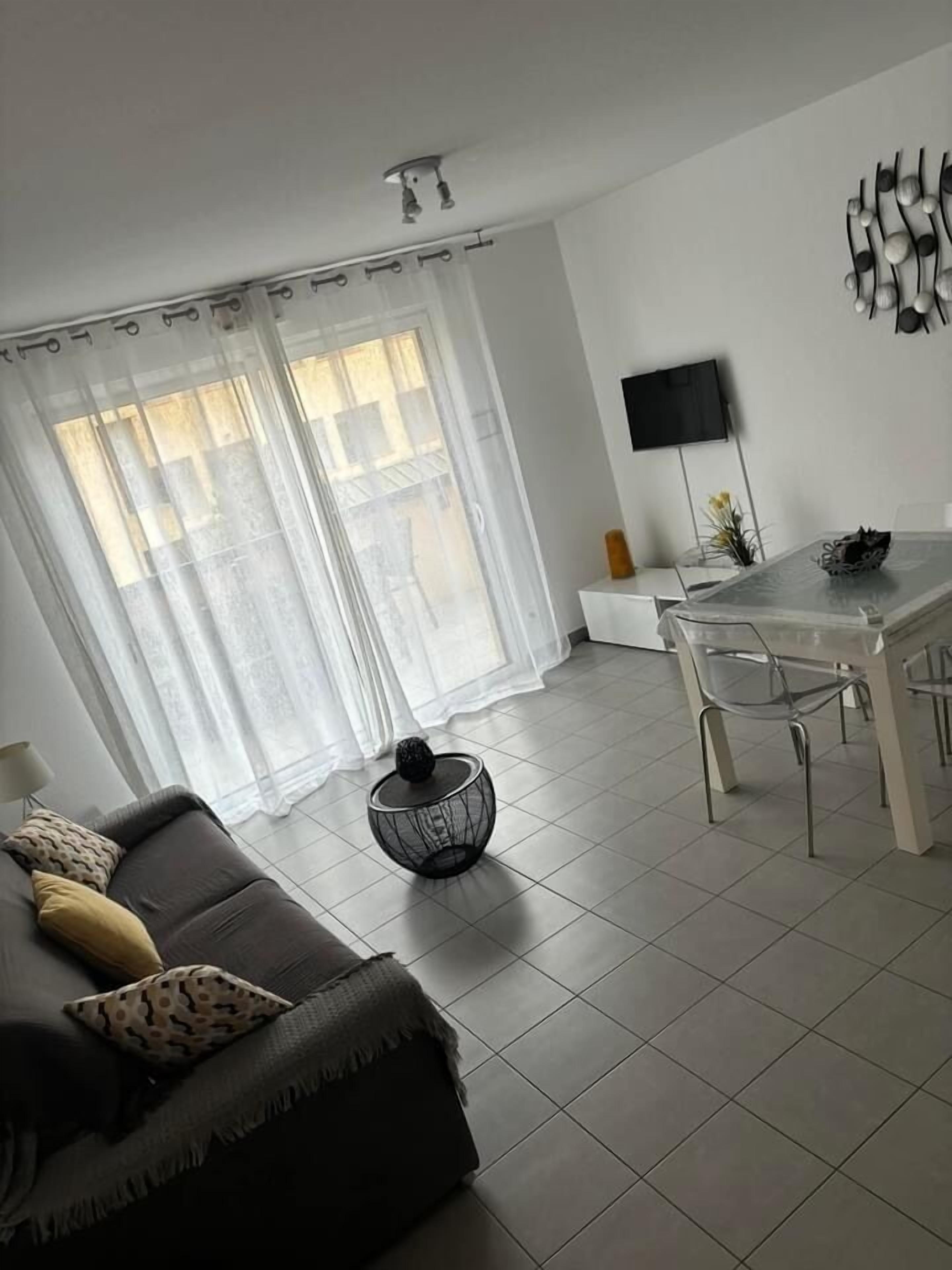 Un salon moderne avec un canapé gris, une table basse ronde et un coin repas comprenant une table et des chaises en verre.