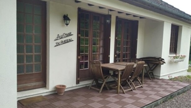 A building with a sign reading 'Au Coeur Du Bateau,' featuring large windows, a covered patio with a table and chairs, and a small planter with flowers.