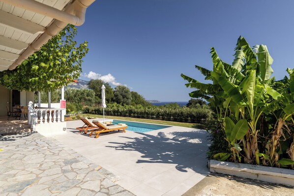 A pool area with lounge chairs, a stone patio, and a view of the sea. - Green retreat ,family friendly , sea view, privacy, picturesque village (spartia)
