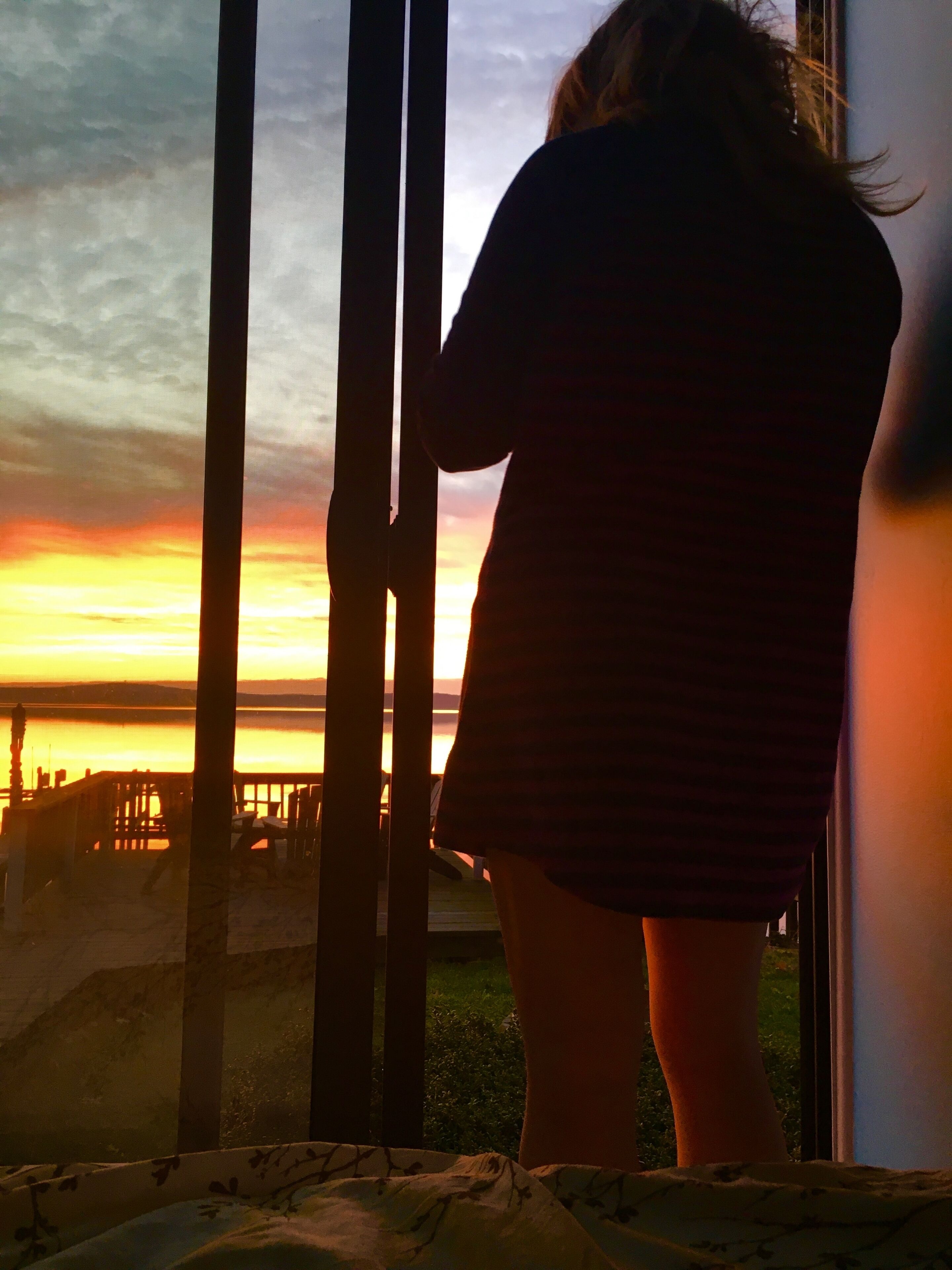 A person standing by a window overlooking a sunset.