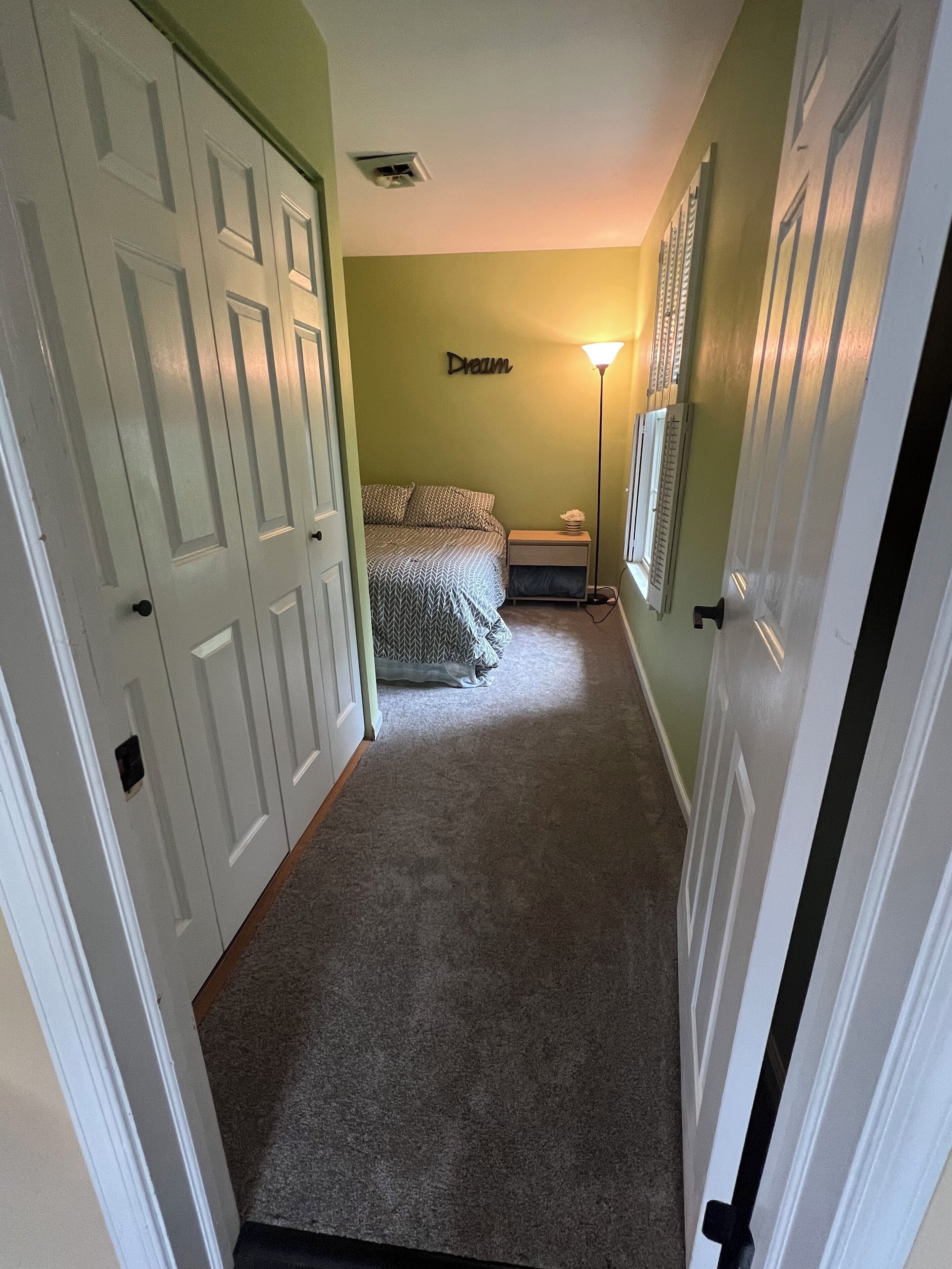 Een gang die leidt naar een slaapkamer met een bed, een nachtkastje en een lamp.