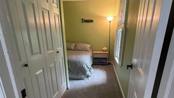 Een gang die leidt naar een slaapkamer met een bed, een nachtkastje en een lamp.