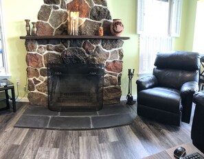 A stone fireplace with a mantel shelf, a leather armchair, and a wooden floor.