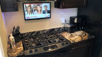 A kitchen with a gas stove, a toaster, and a flat-screen TV mounted above the stove displaying a news channel.