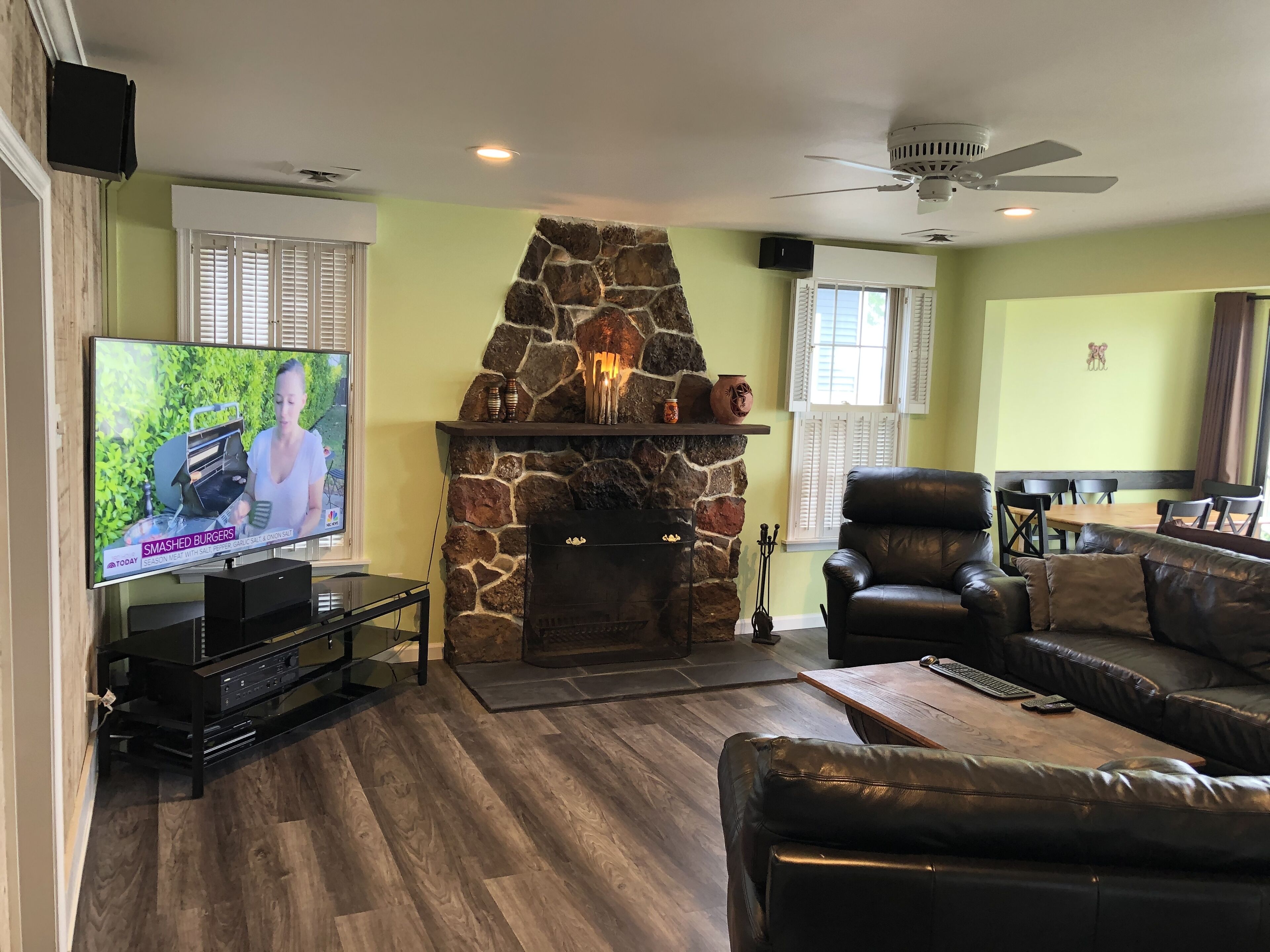 A living room with a stone fireplace, a television, leather furniture, and a ceiling fan.