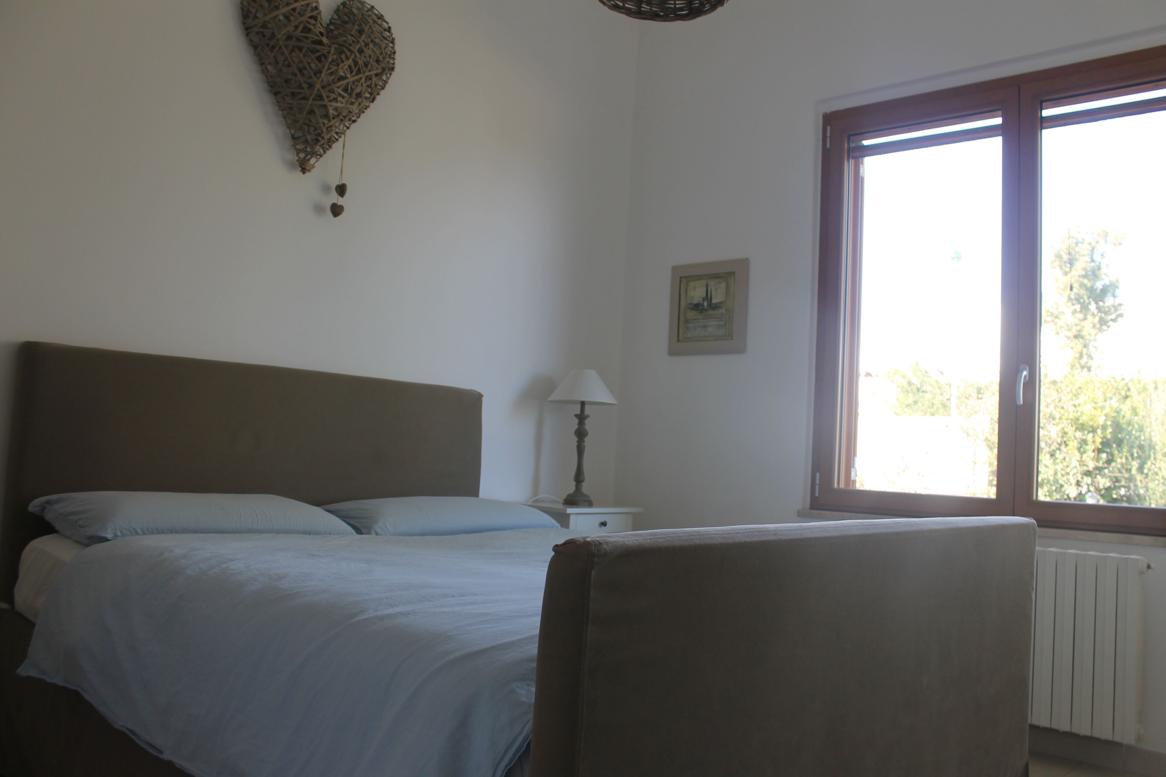 Une chambre à coucher comprenant un lit, une chaise, une table de chevet, une lampe, une fenêtre et un élément de décoration murale.
