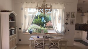 Un comedor con mesa, sillas, una araña y una ventana con cortinas.