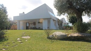 Una casa moderna con techo inclinado, un árbol grande en el jardín delantero y un cielo despejado.