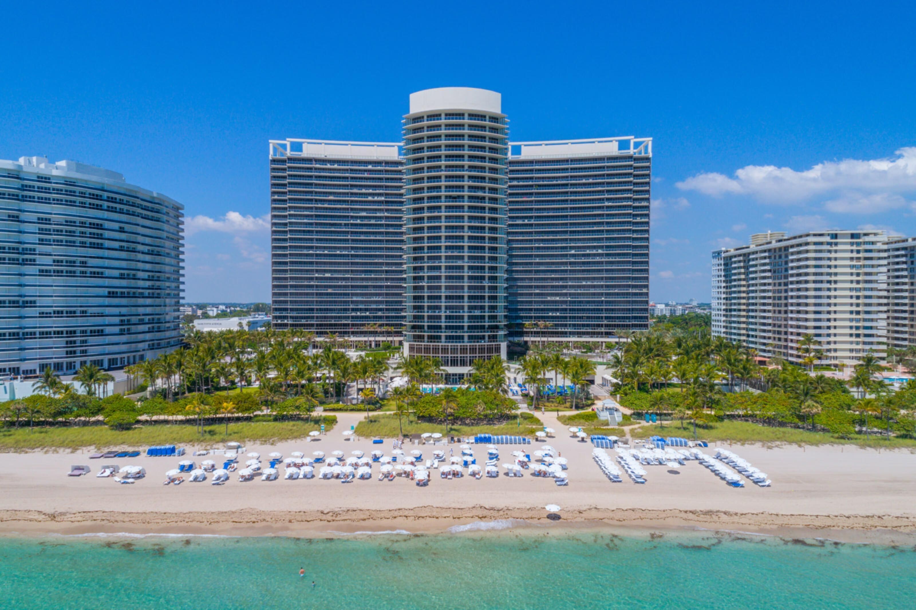 Un hotel frente a la playa con fachada curva, varios balcones y una zona de piscina con sombrillas.