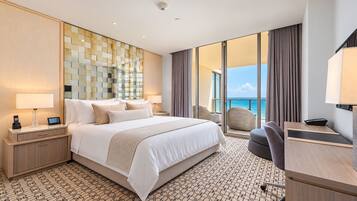 Een hotelkamer met een groot bed, een bureau, een stoel, een telefoon en uitzicht op zee.