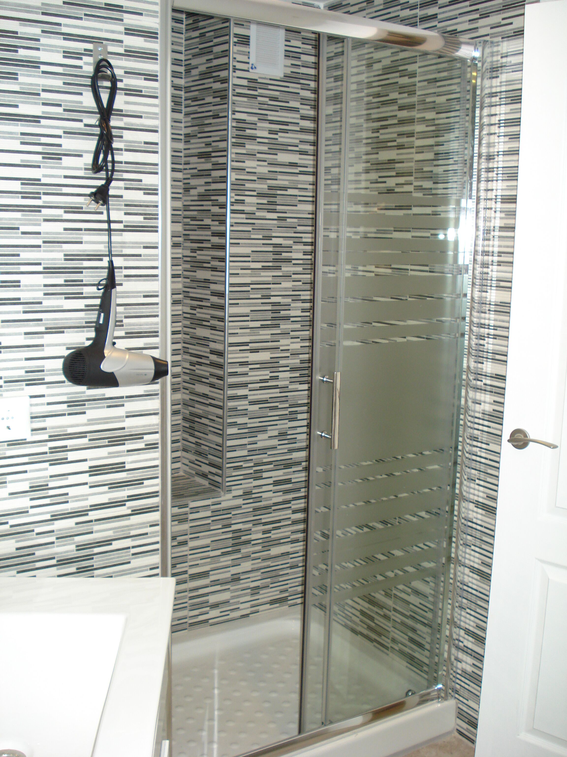 Un baño con mampara de vidrio, un perchero y un papel tapiz decorado.