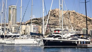 A marina with several yachts docked, a rocky hill in the background, and a tall building with a sign. - APART.RIVERA #3 IN THE OLD TOWN ONLY 10 MINUTES WALKING DISTANCE TO THE BEACH. (Alicante)