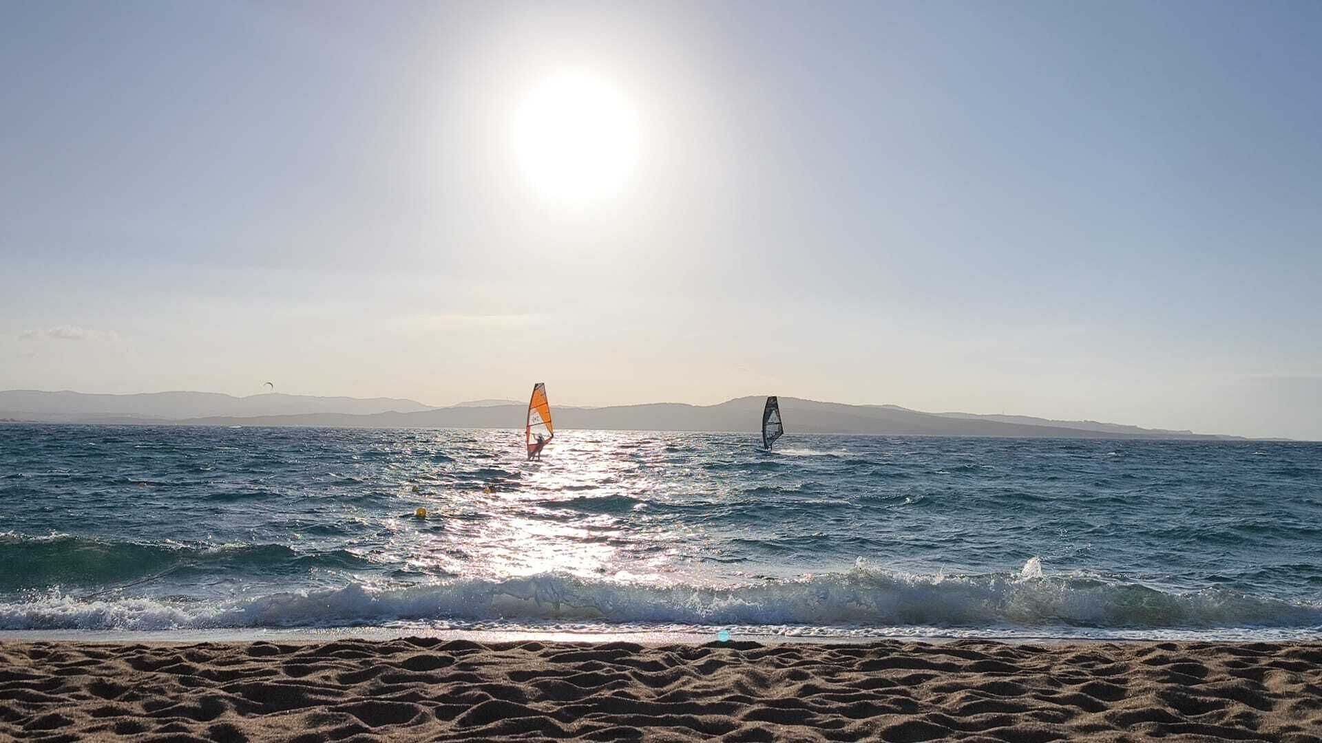 Una playa con dos windsurfistas y un cielo despejado.