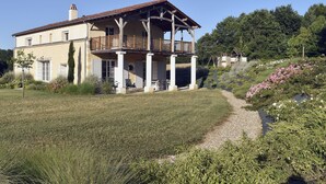 Una casa a due piani con un balcone, immersa in un giardino ricco di piante e fiori.