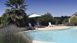 Una piscina con lettini e ombrelloni, circondata da palme e piante di lavanda.