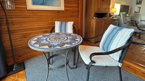 Ein gemütlicher Raum mit einem runden Mosaiktisch, einem gestreiftem Sitzhocker und einer Holzkommode.