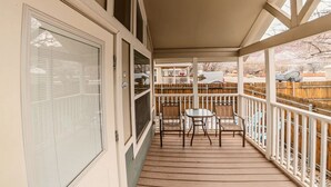 A covered porch with a wooden deck, a white railing, and a table with chairs. - Pet-Friendly Tiny Home Near Arches | Sleeps 6 | Fenced Yard | Sunset Mesa (Moab)