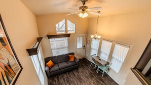A compact living space with a dark wood floor, a gray sofa with orange cushions, a dining table with chairs, and a ceiling fan. - Pet-Friendly Tiny Home Near Arches | Sleeps 6 | Fenced Yard | Sunset Mesa (Moab)